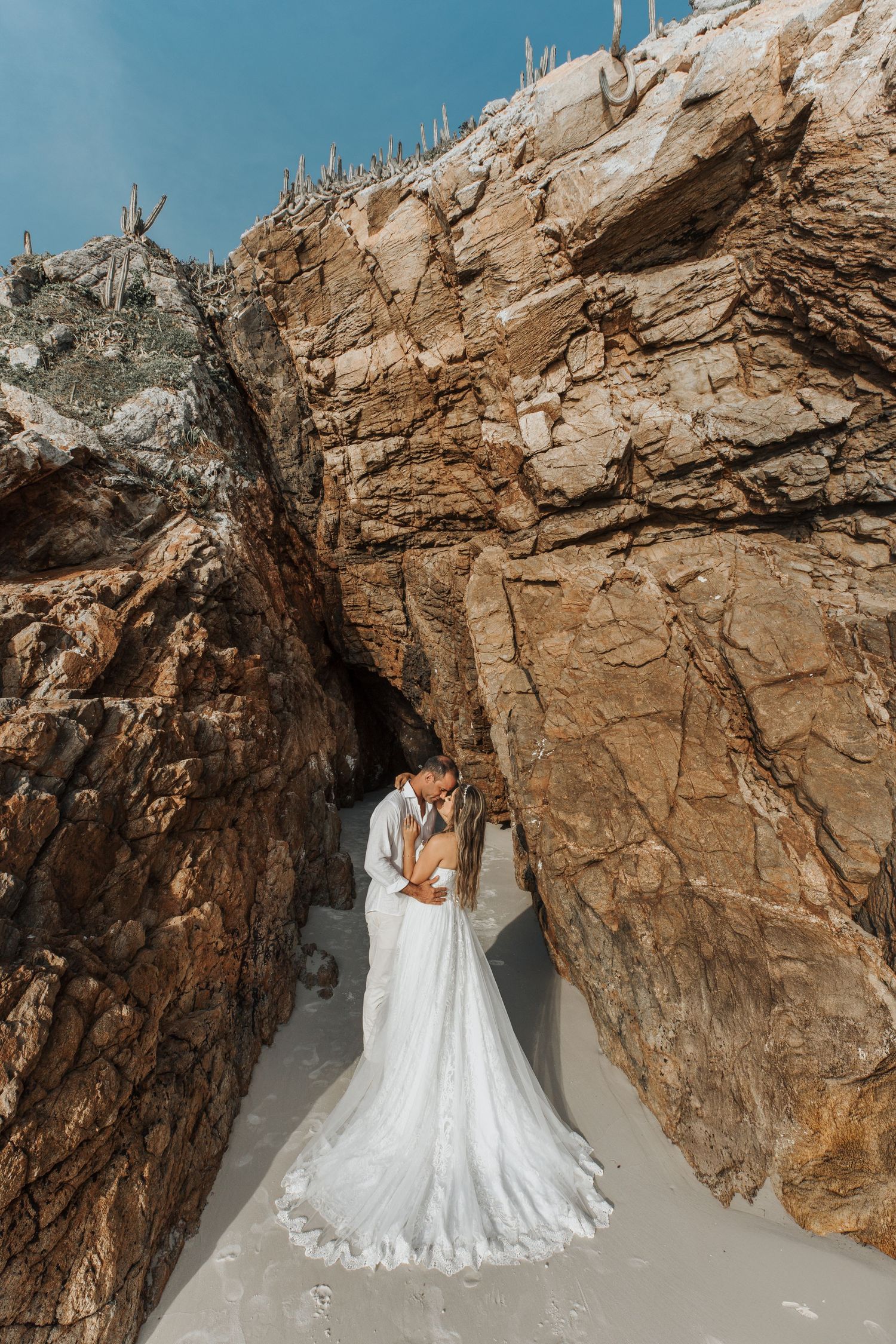 Wedding couple embracing in dramatic rocky cave setting with flowing white dress.