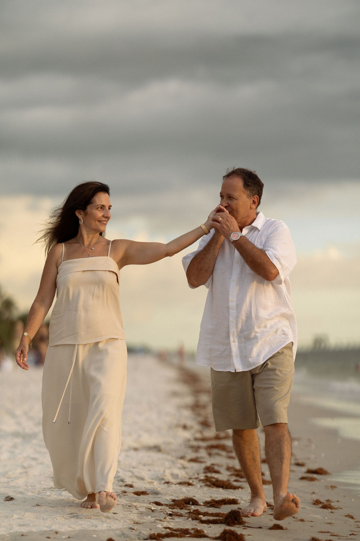 Beach engagement session with flowing white dress against stormy sky.