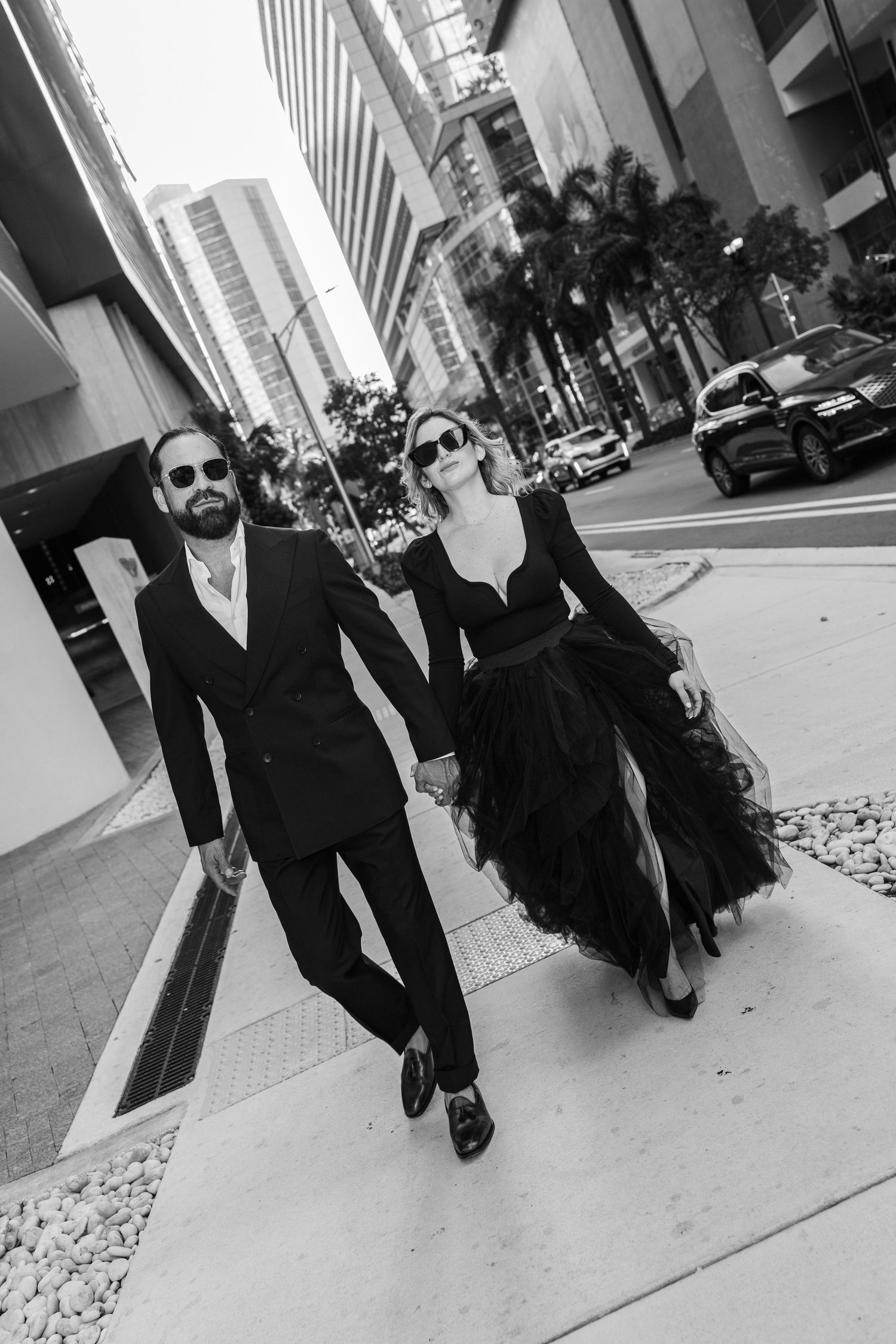 Stylish couple in black attire walking along urban sidewalk.