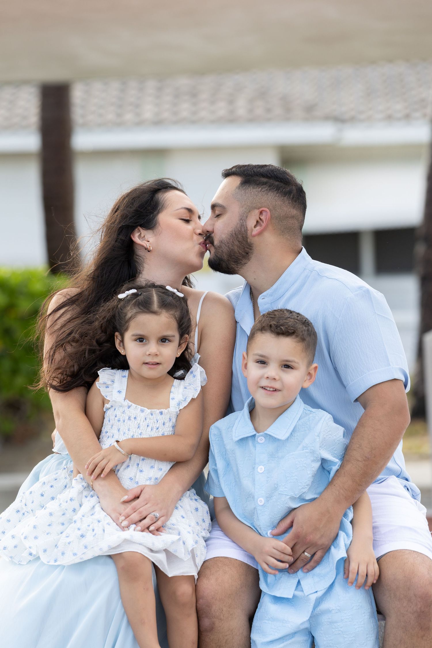 Family wearing coordinated blue and white outfits share tender moments in a series of intimate portraits.