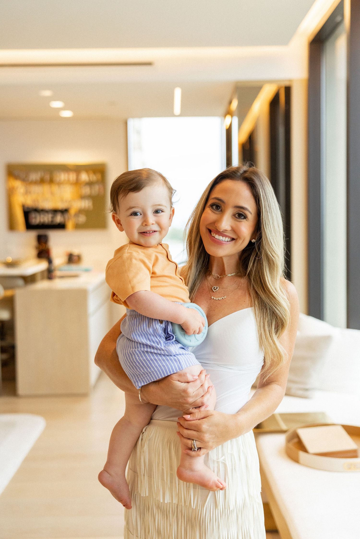 A parent holds a baby wearing blue and white striped clothing in a bright modern home interior.