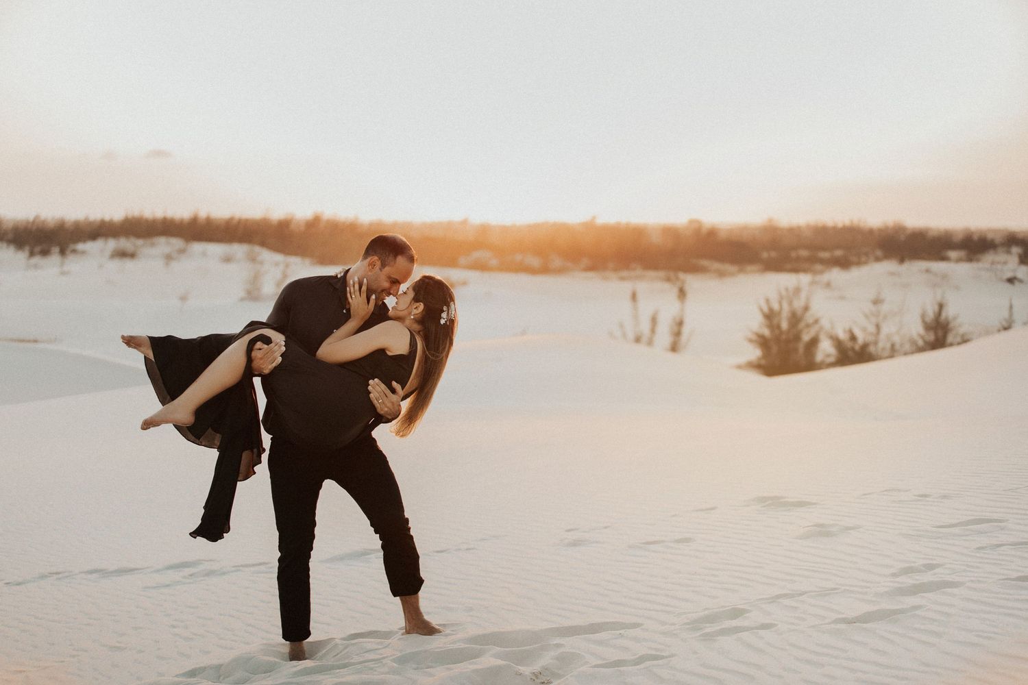 A couple poses playfully in the white sand during their wedding photoshoot.