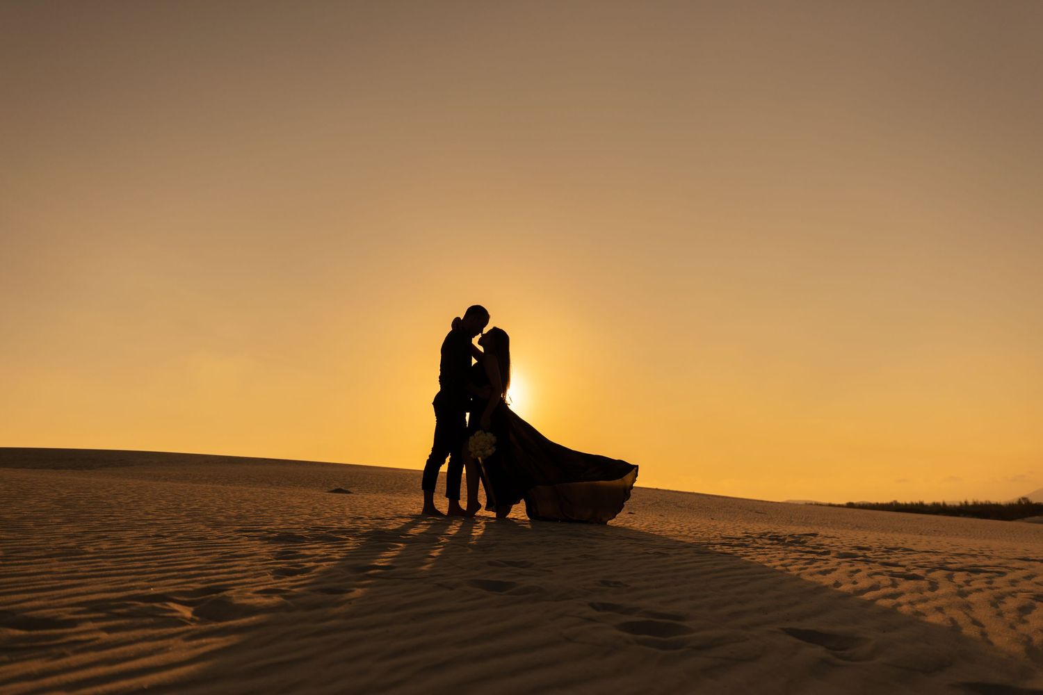 Silhouettes of a couple on sand dunes during a golden sunset.