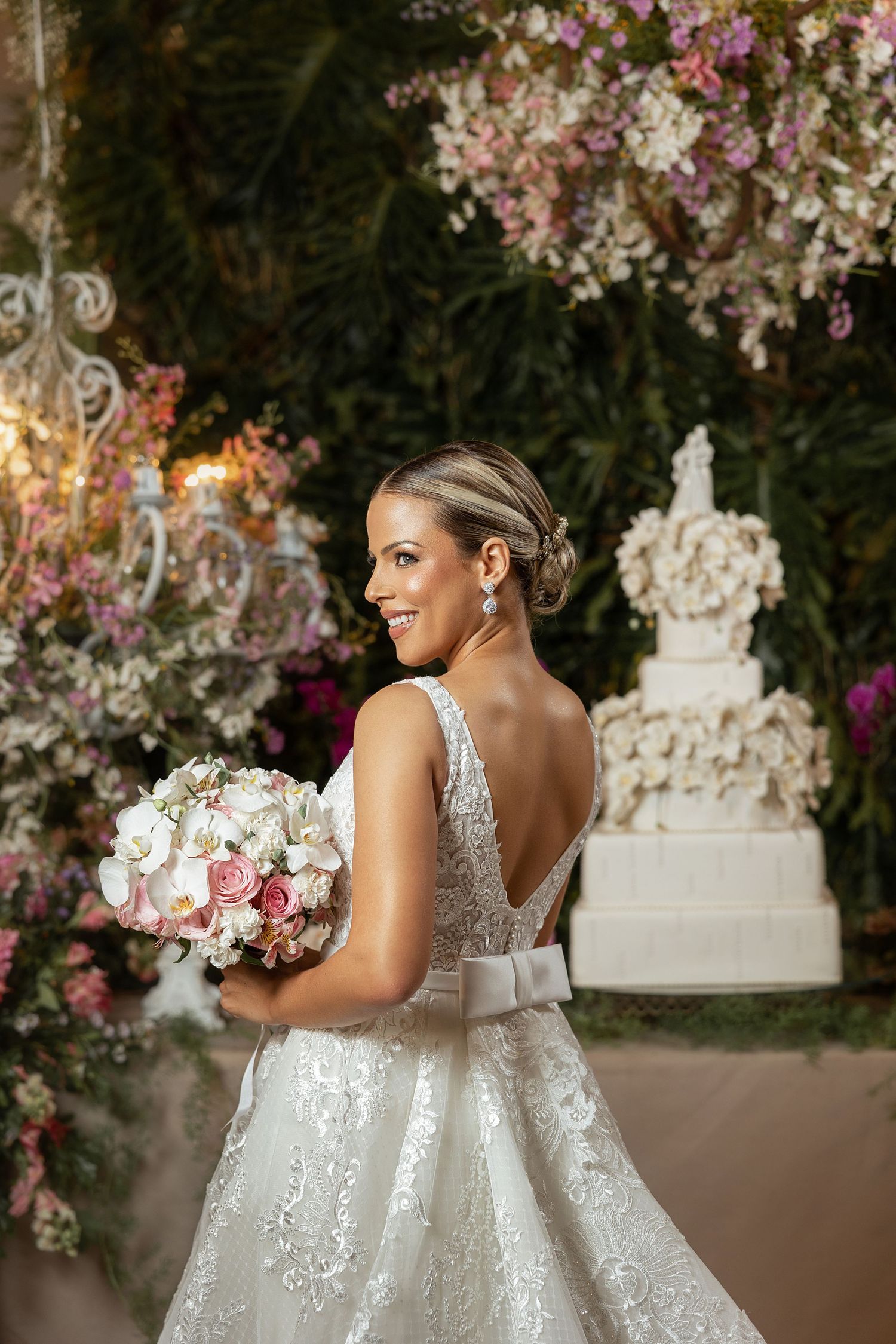 Elegant wedding setup with floral arrangements and crystal chandeliers and a bride with her back turned to the camera.