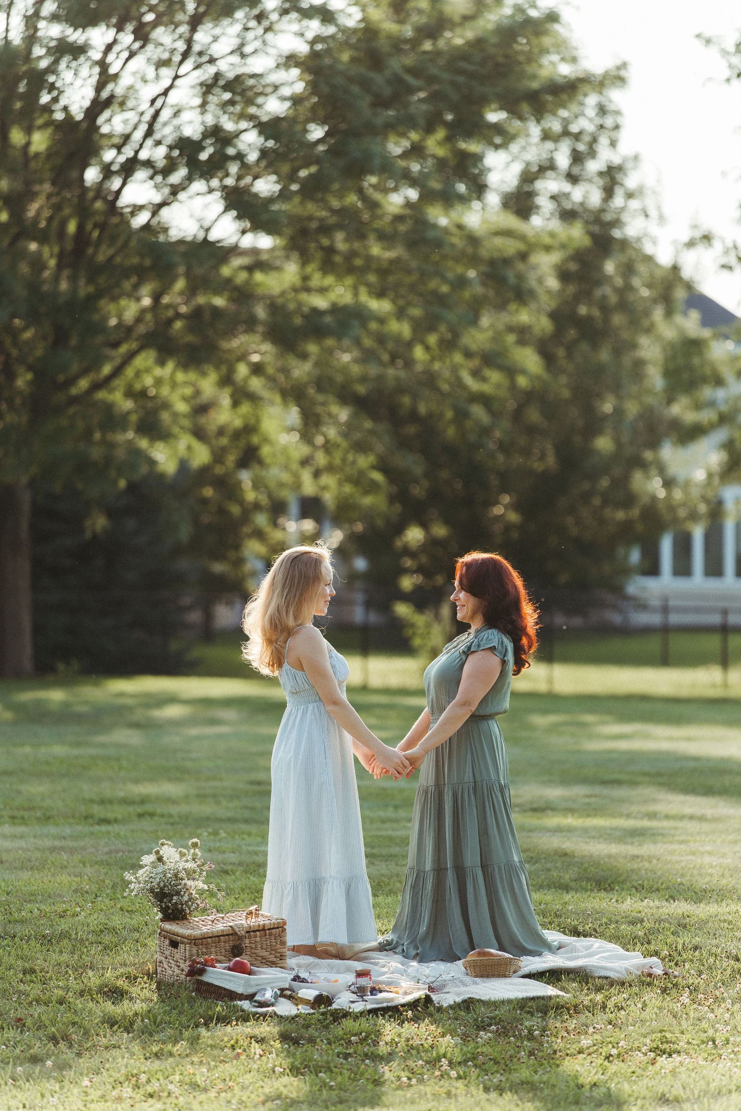 Two women who are mother and daughter sharing intimate conversation during sunset picnic on grass.