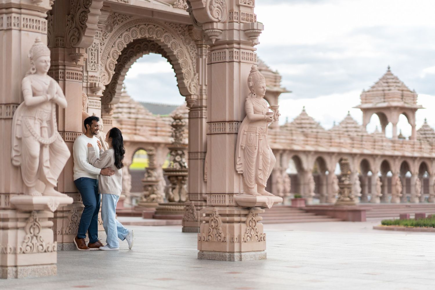 Ornate stone archways and pillars line a covered walkway at an elaborate Hindu temple complex in India.