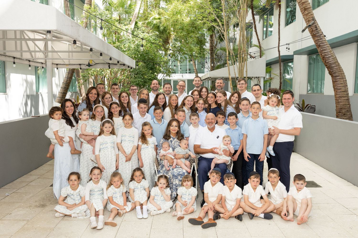 Large family group photo with multiple generations wearing coordinated white outfits outdoors.