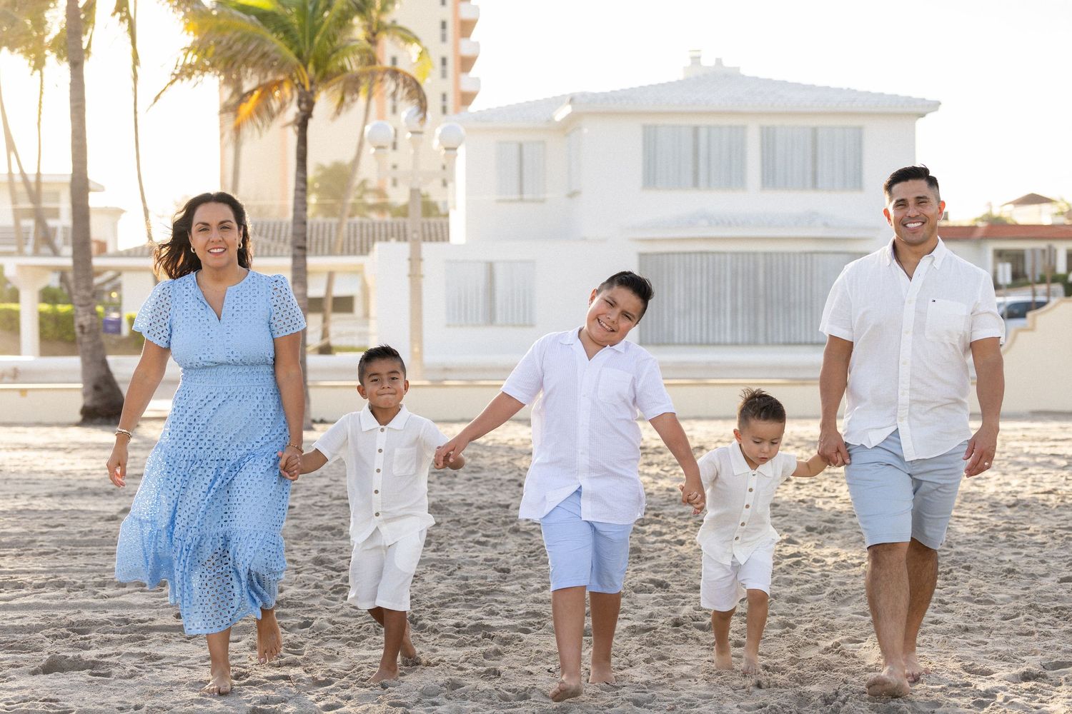 A series of beach photos showing a family in white and blue outfits walking and playing on the sand at sunset.