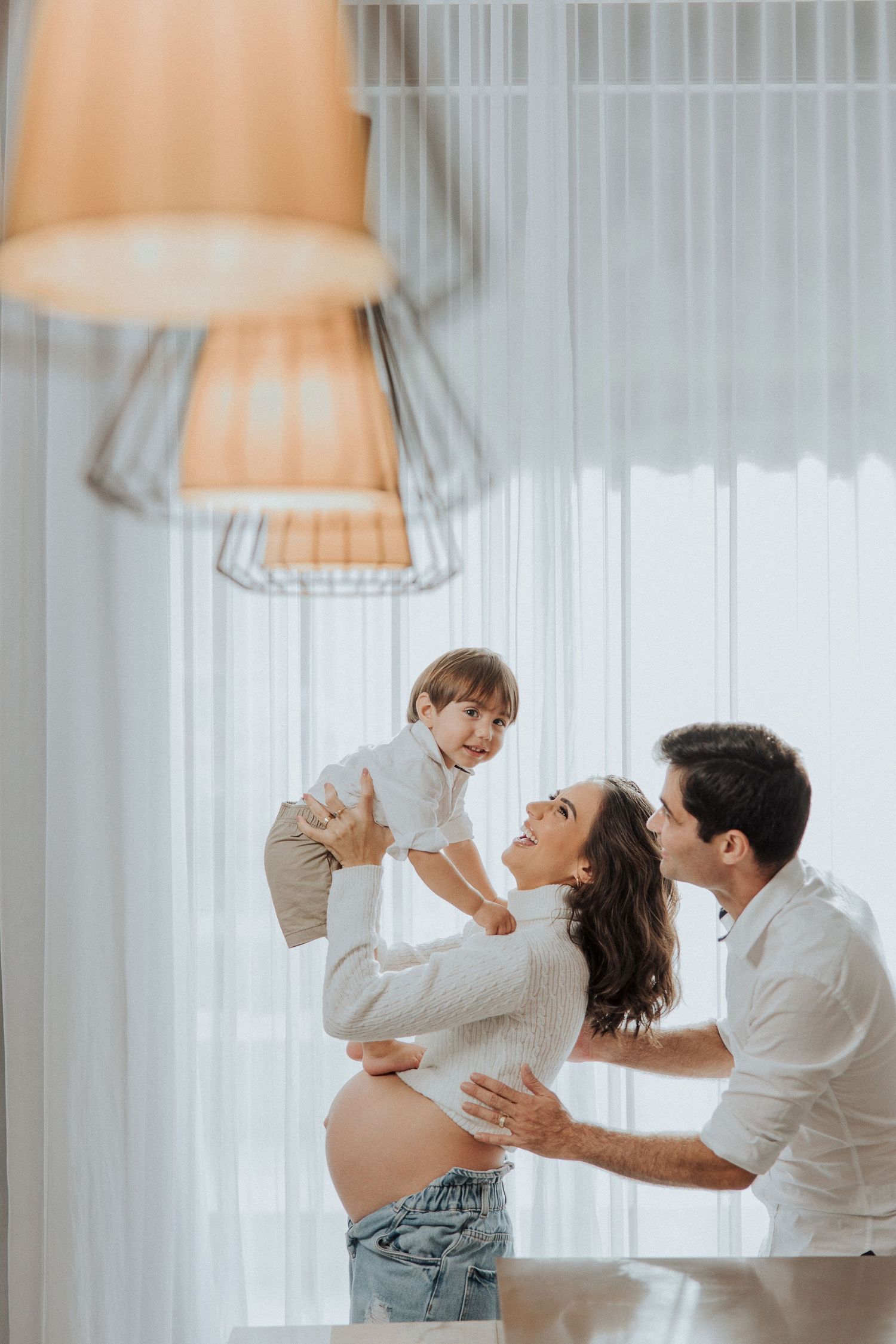 Playful indoor couple photoshoot with white curtains and pendant lighting.