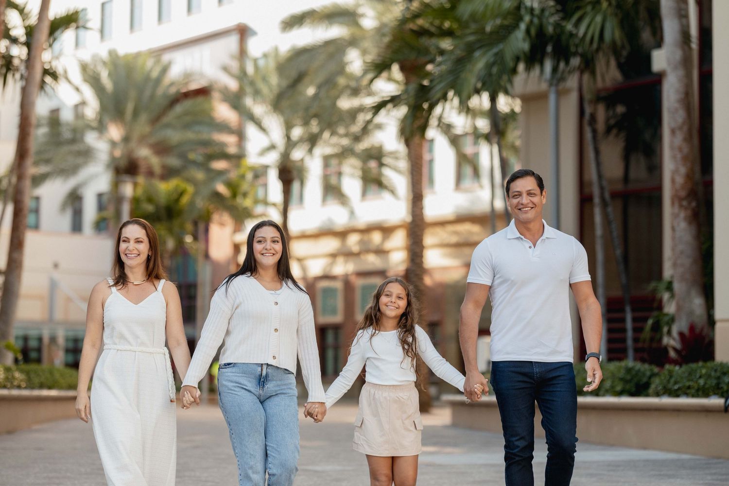 Family walking together on palm tree lined path in coordinated white outfits in West Palm Beach.
