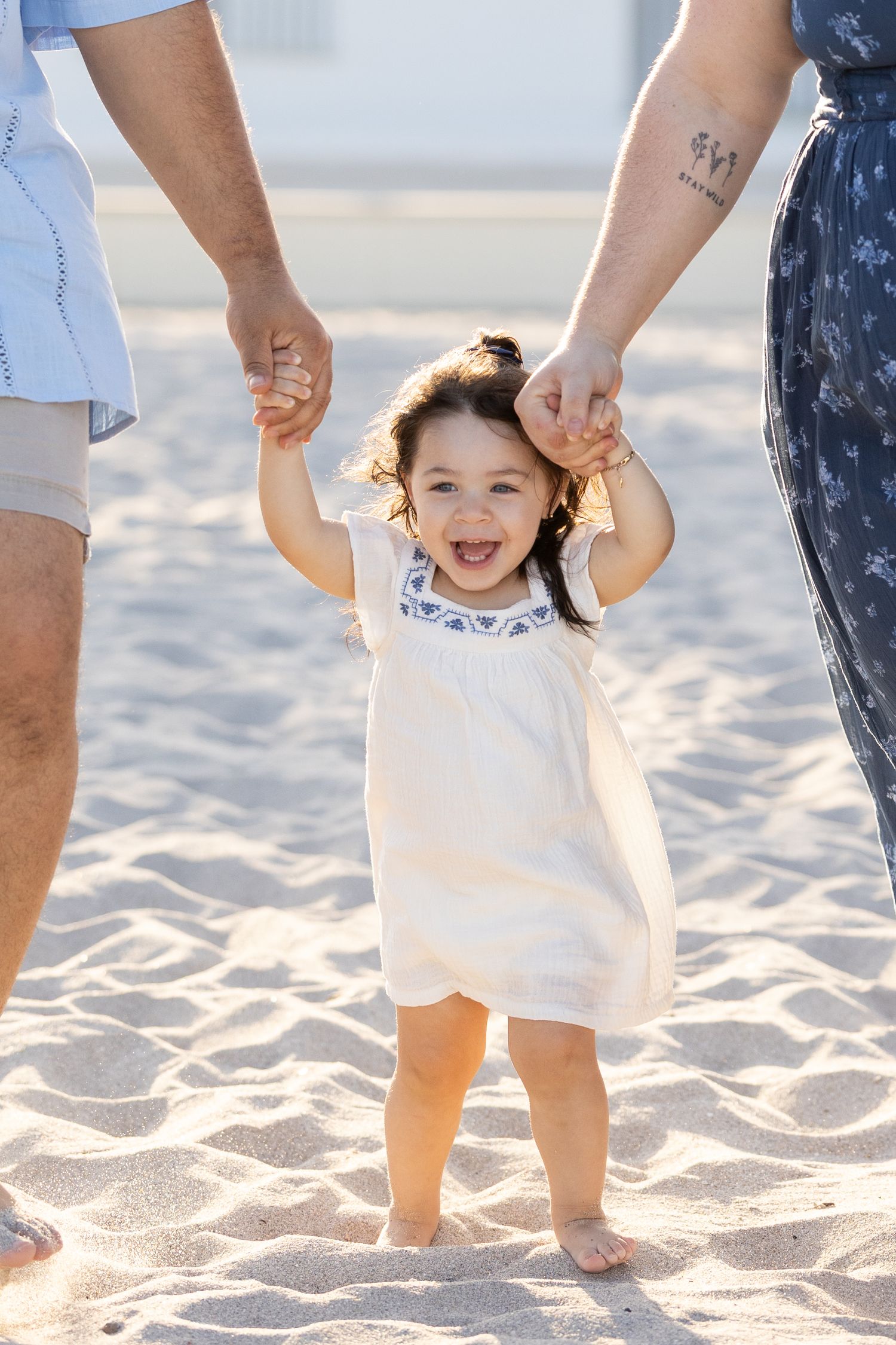 Close-up of feet walking together on sandy beach with a toddler happily smiling holding hands.