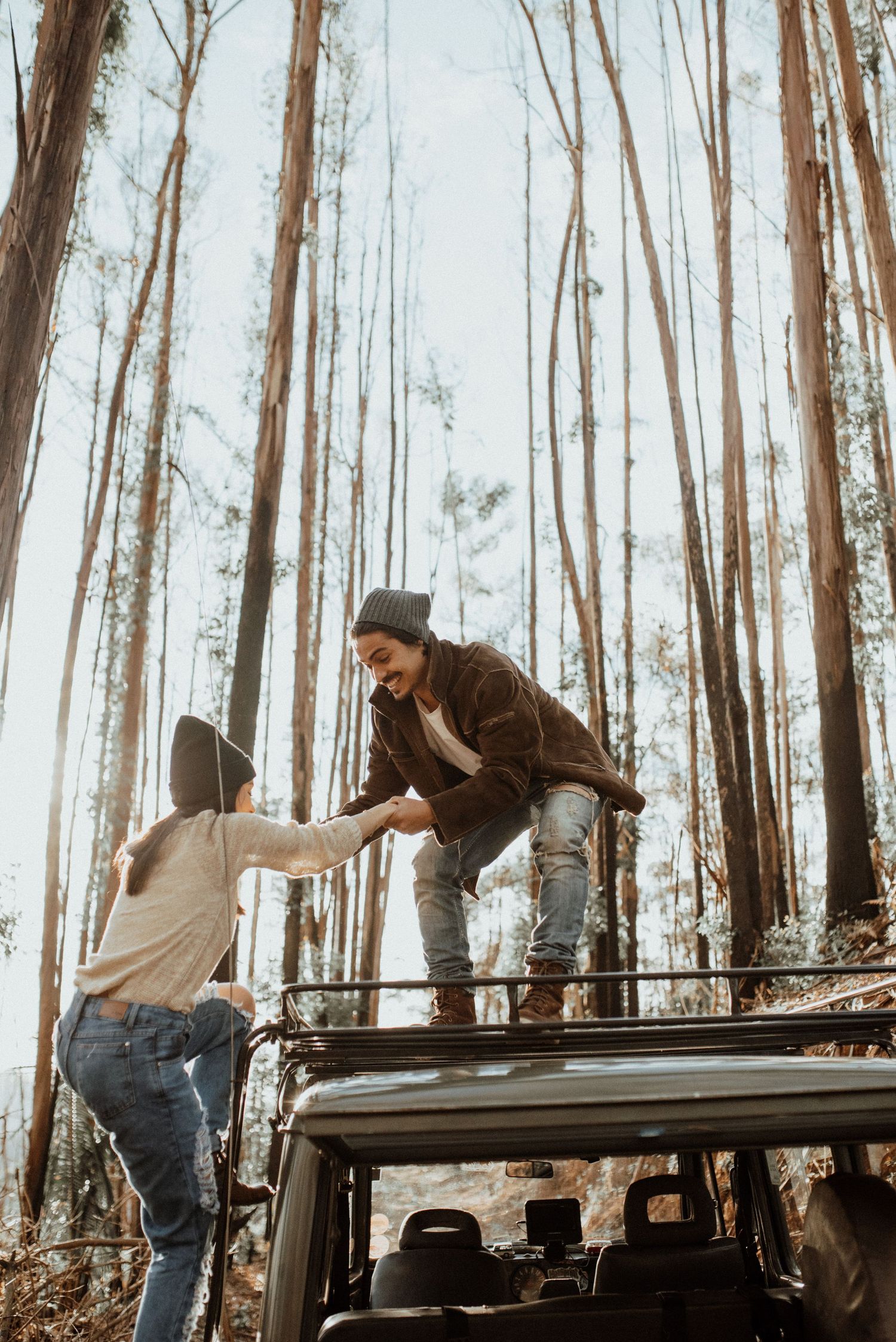 Friends climbing on top of vintage car in wooded area during adventure photoshoot.