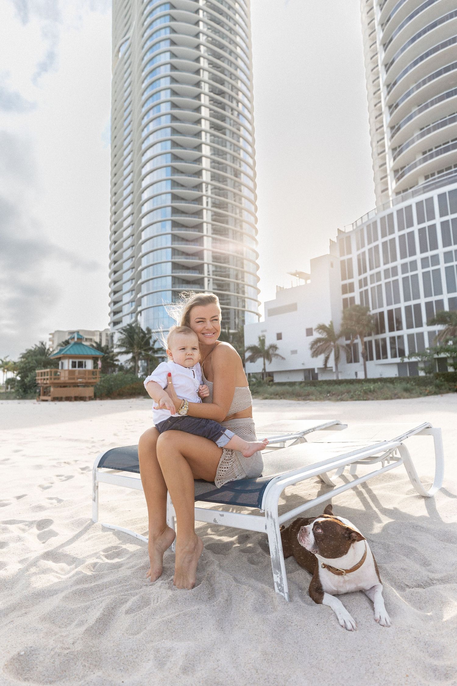Beachside portrait session with a dog on a white lounge chair near modern high-rise buildings.