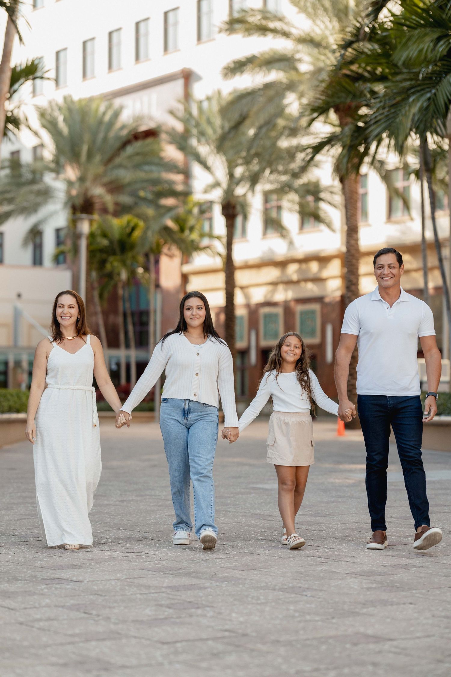 Family walking together in coordinated white outfits along palm-lined promenade.