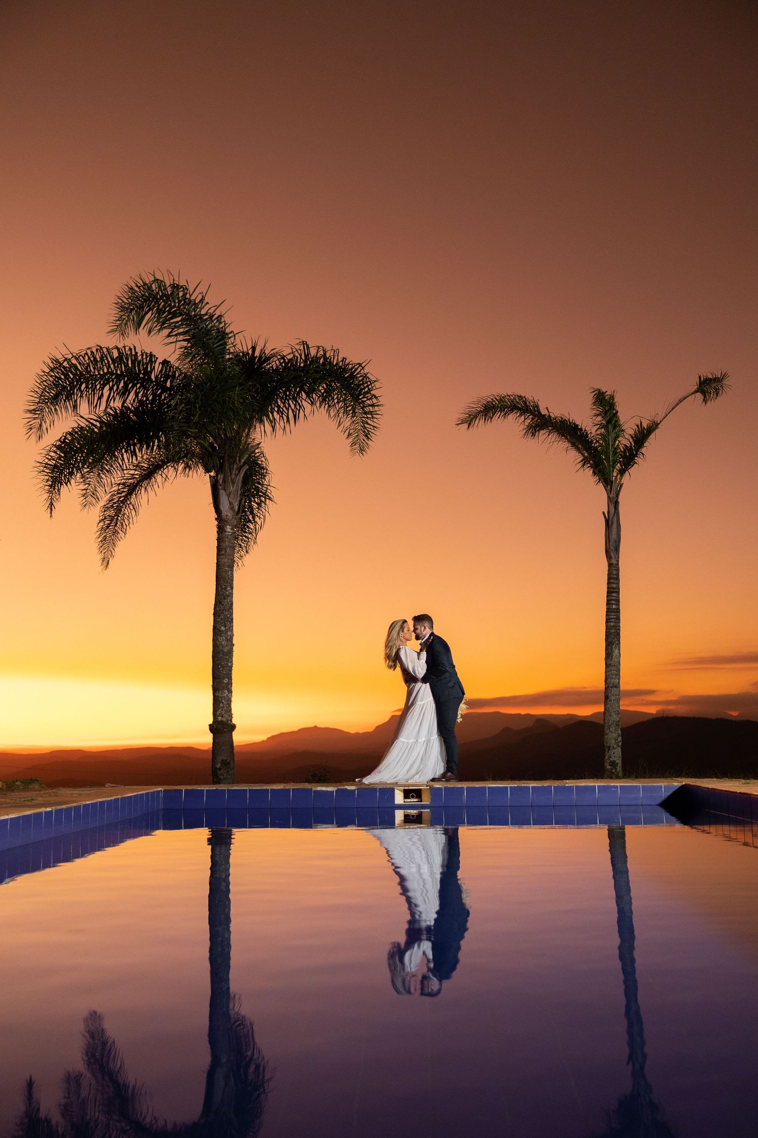 Romantic sunset wedding portrait with palm trees and infinity pool silhouette.