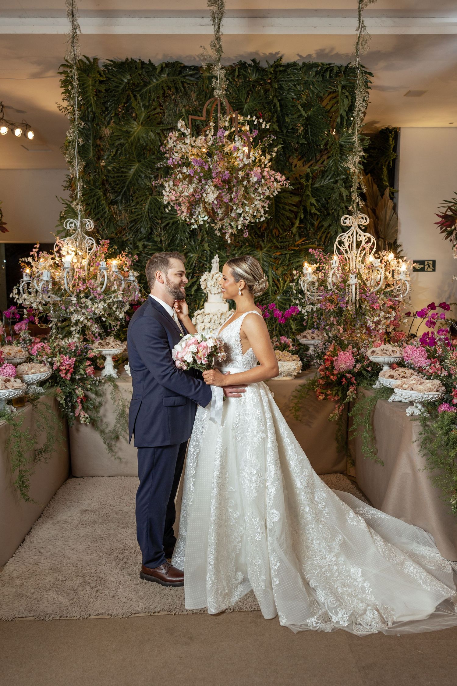Wedding couple poses under floral chandeliers and greenery decorations.