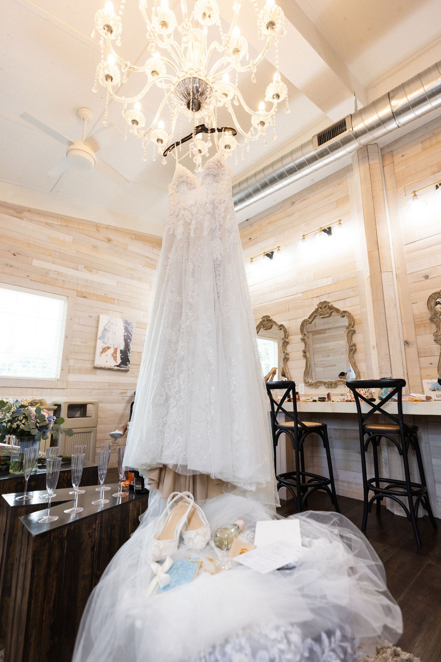 Elegant white wedding dress hanging from chandelier in rustic wooden room with vintage decor.