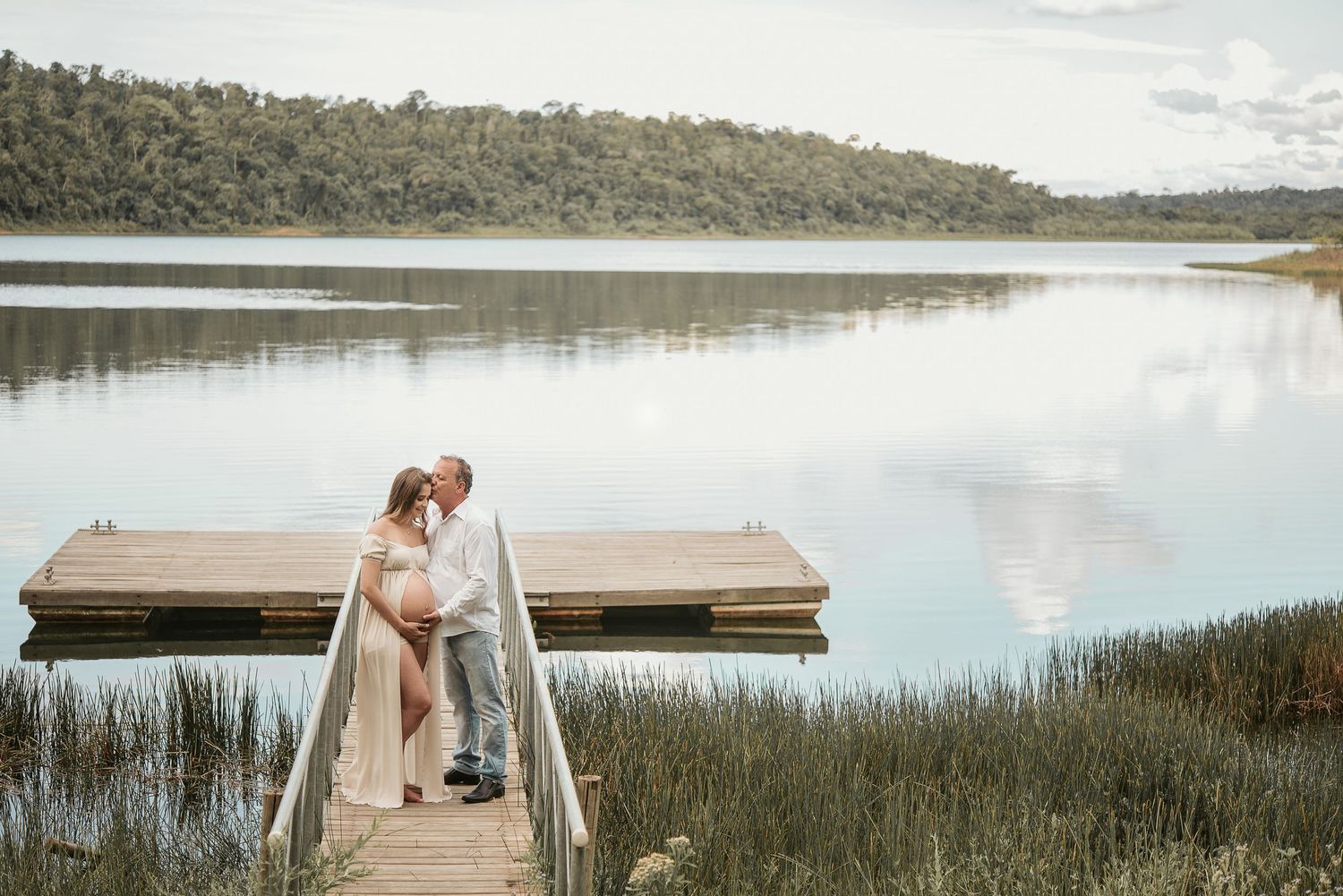 Romantic couple photos taken on a wooden dock by a serene lake surrounded by marsh grass at sunset.