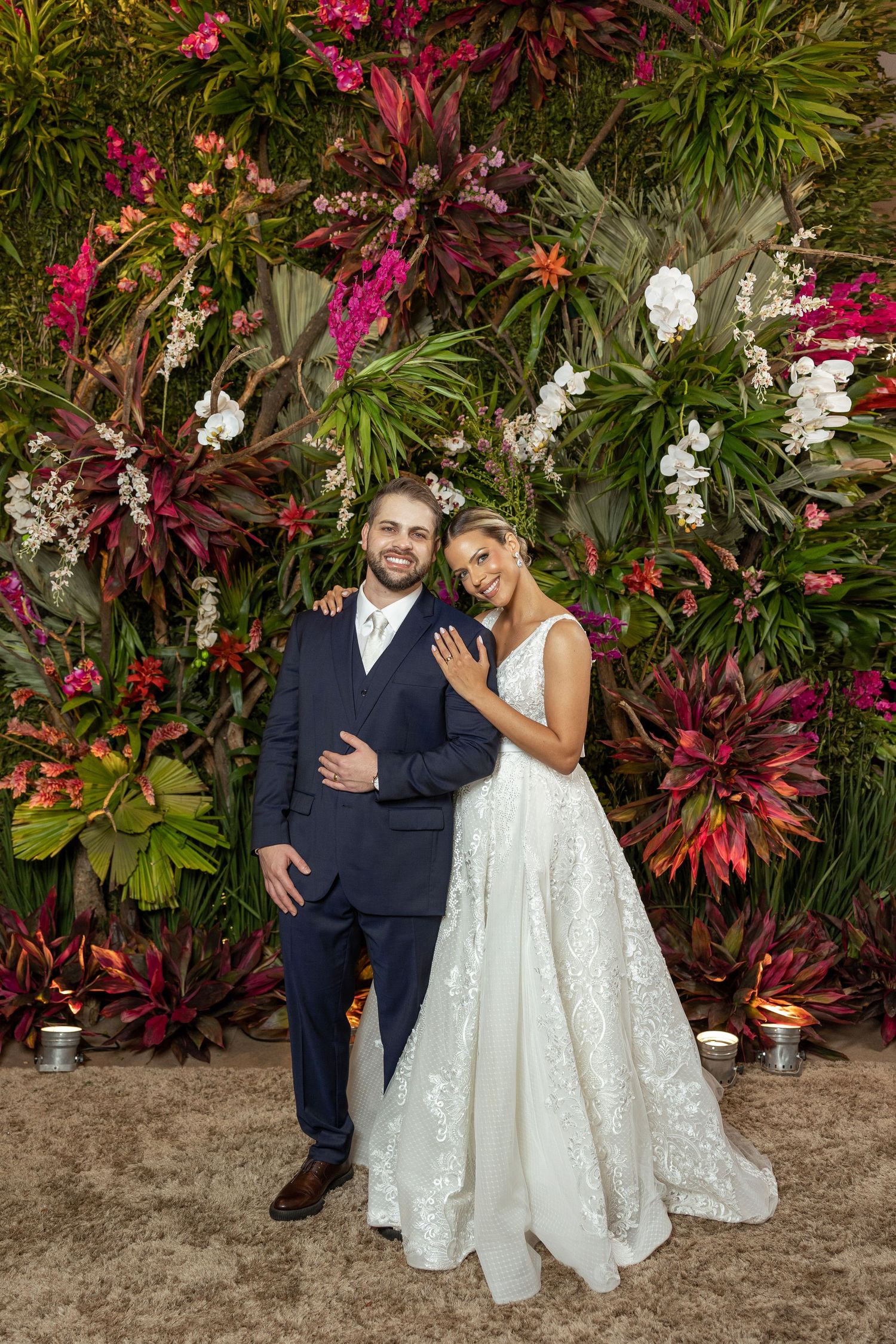 Wedding couple posed against vibrant tropical garden with pink and white flowers.