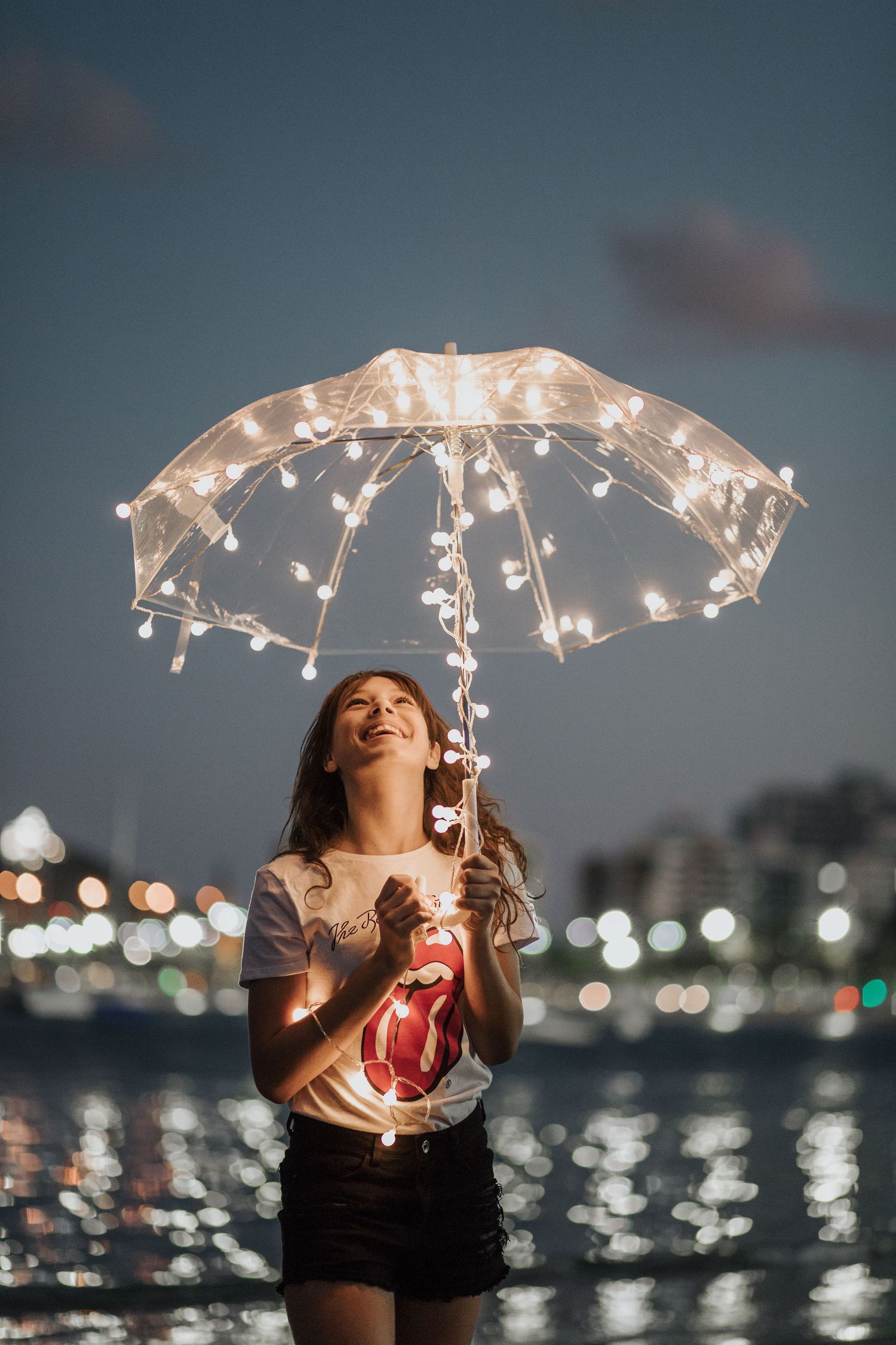 Nighttime portrait session with illuminated umbrella creating magical lighting effects over water.