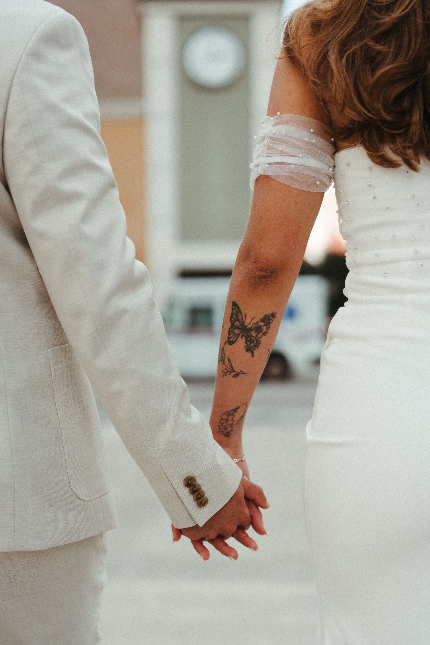 Close-up view of hands with tattoos wearing white formal attire during a wedding ceremony.