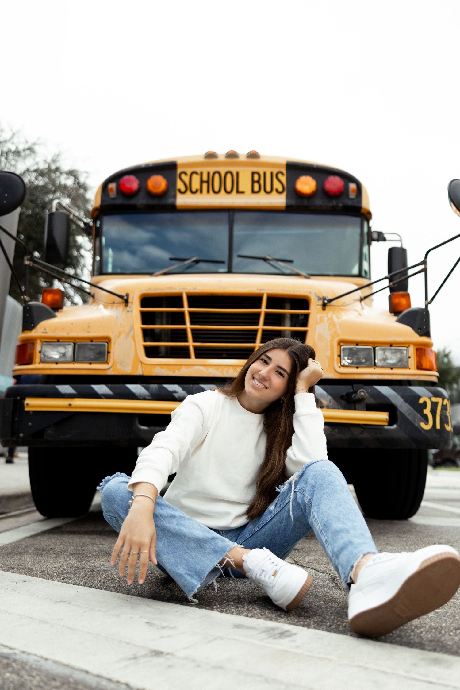 Person in casual attire posing playfully in front of yellow school buses for sweet 16 birthday shoot.