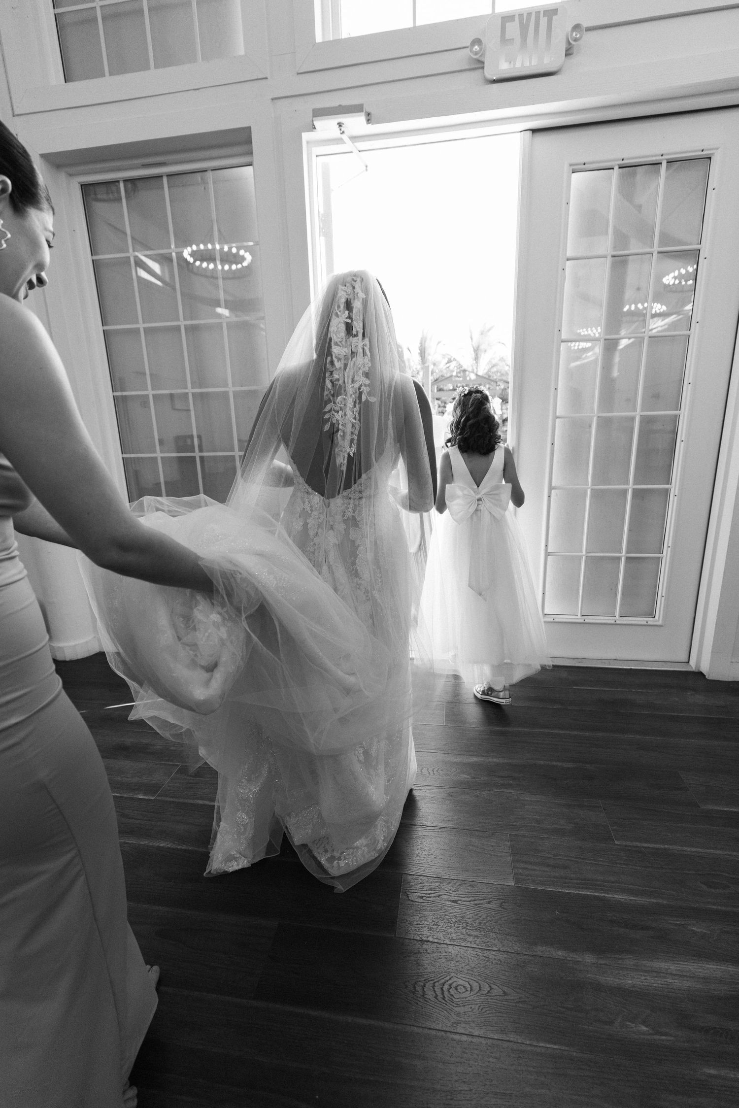 A black and white photo showing a bride with flowing movement with a white dress against dark hardwood floors.