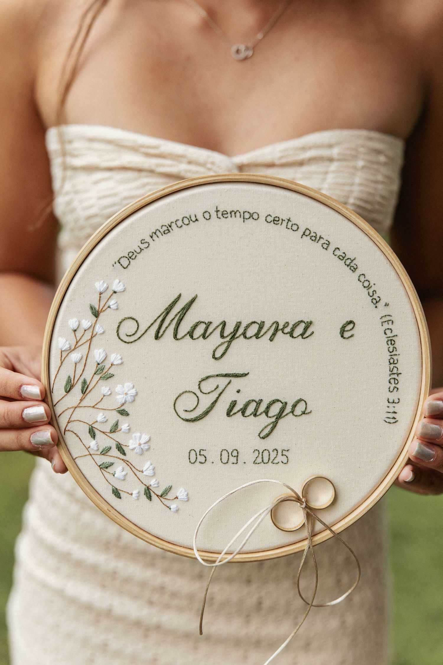 Wedding rings displayed on decorative oval embroidery hoops with delicate floral designs and calligraphy text.