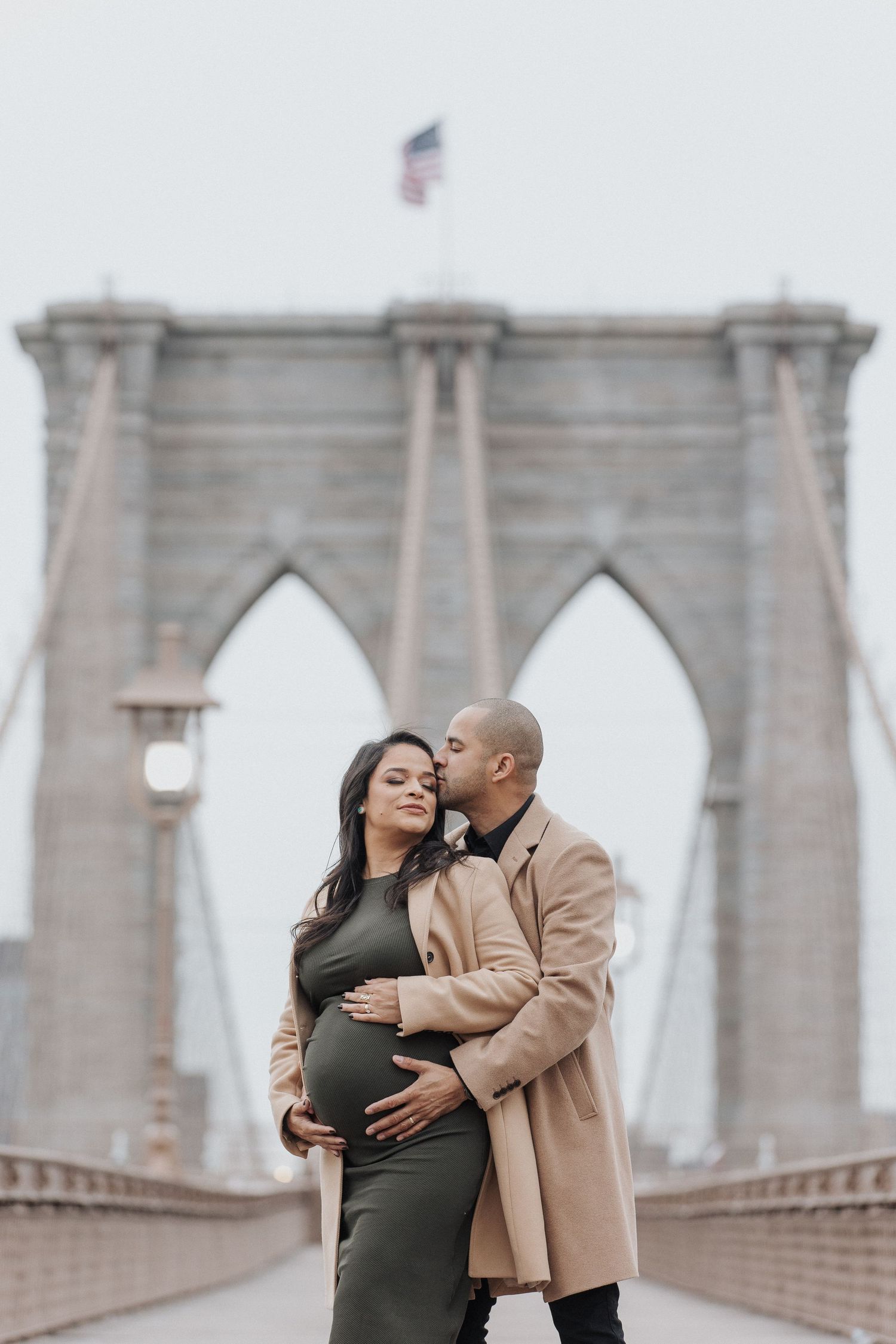 Romantic moment captured at Brooklyn Bridge with iconic architecture in background.