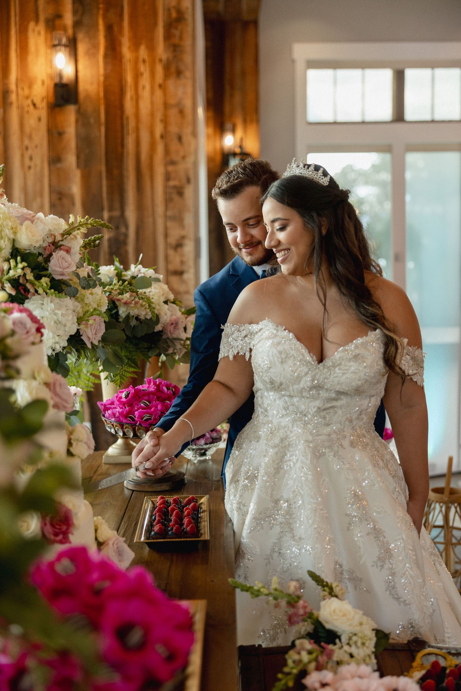 Elegant white lace wedding dress with floral details and pink flower arrangements in a rustic wooden venue.