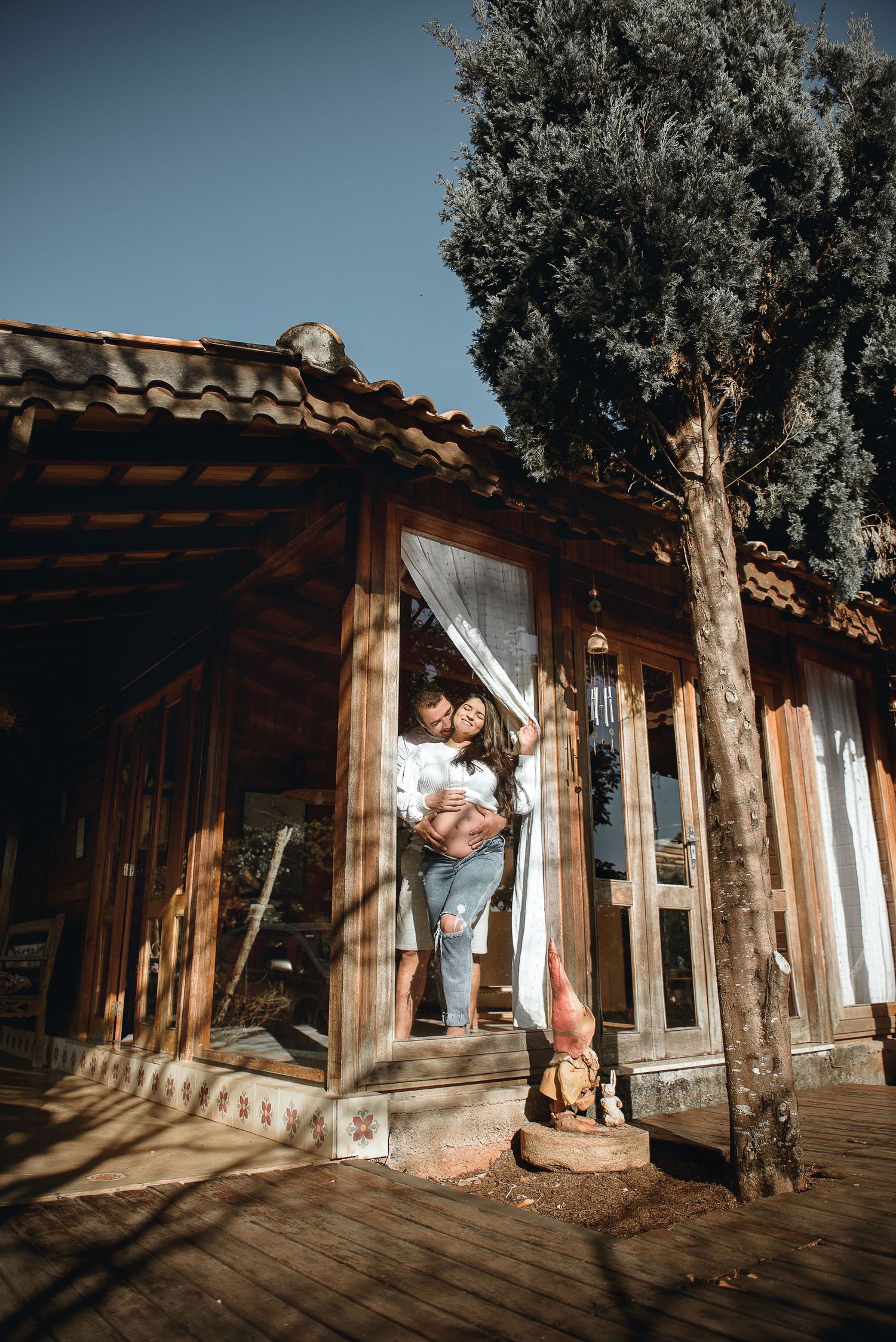 A romantic photoshoot at a rustic wooden porch with sunlight casting shadows through the beams.