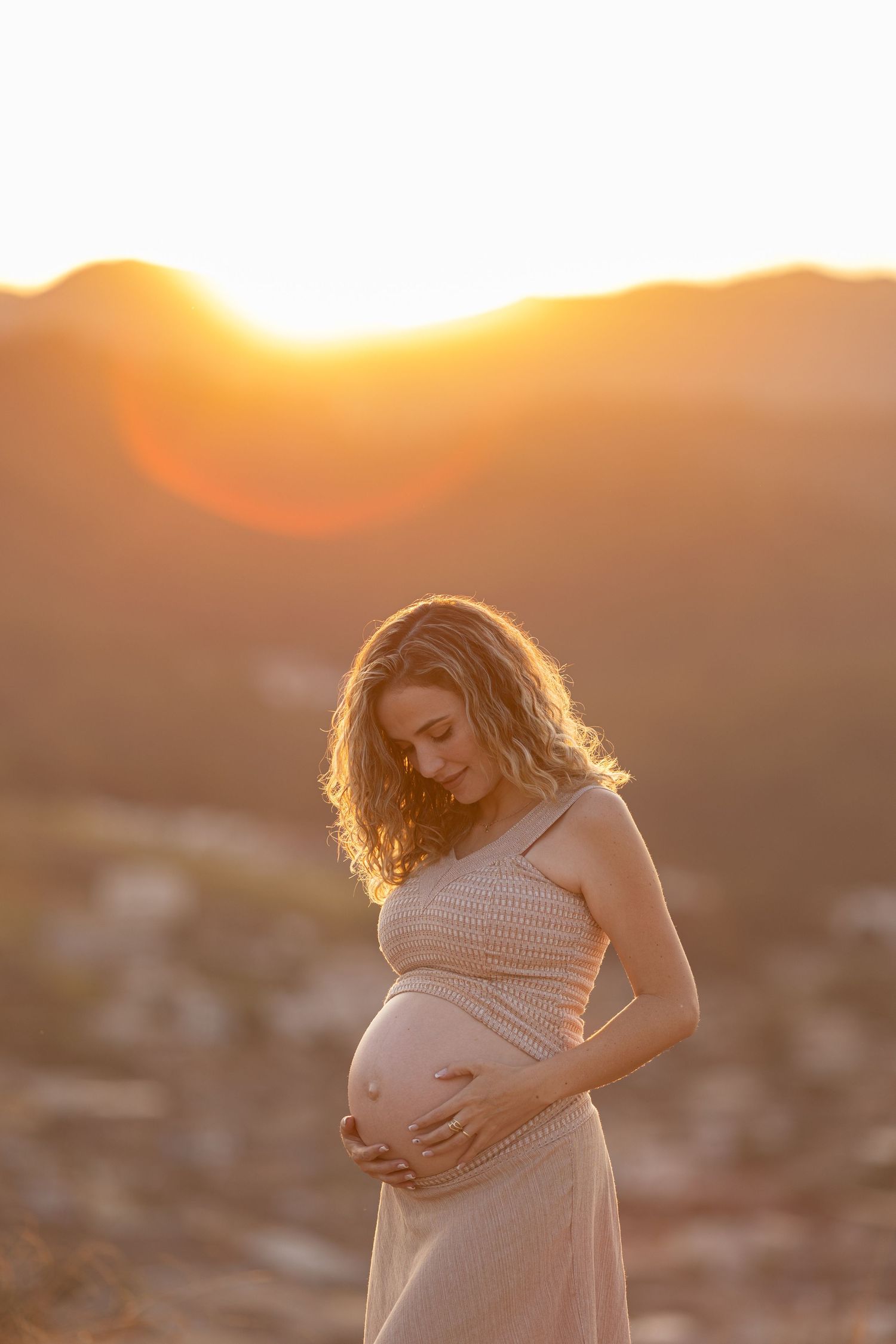 A silhouetted pregnant figure stands against a golden sunset backdrop while holding their belly.