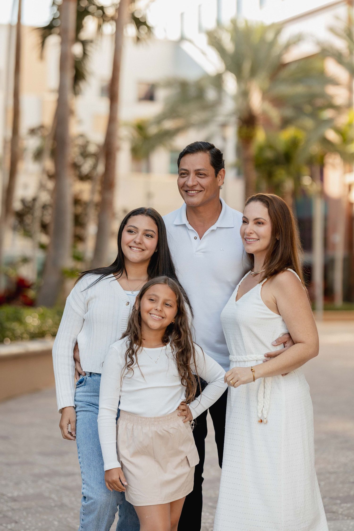 Family of four wearing coordinated white outfits poses together in a tropical setting.