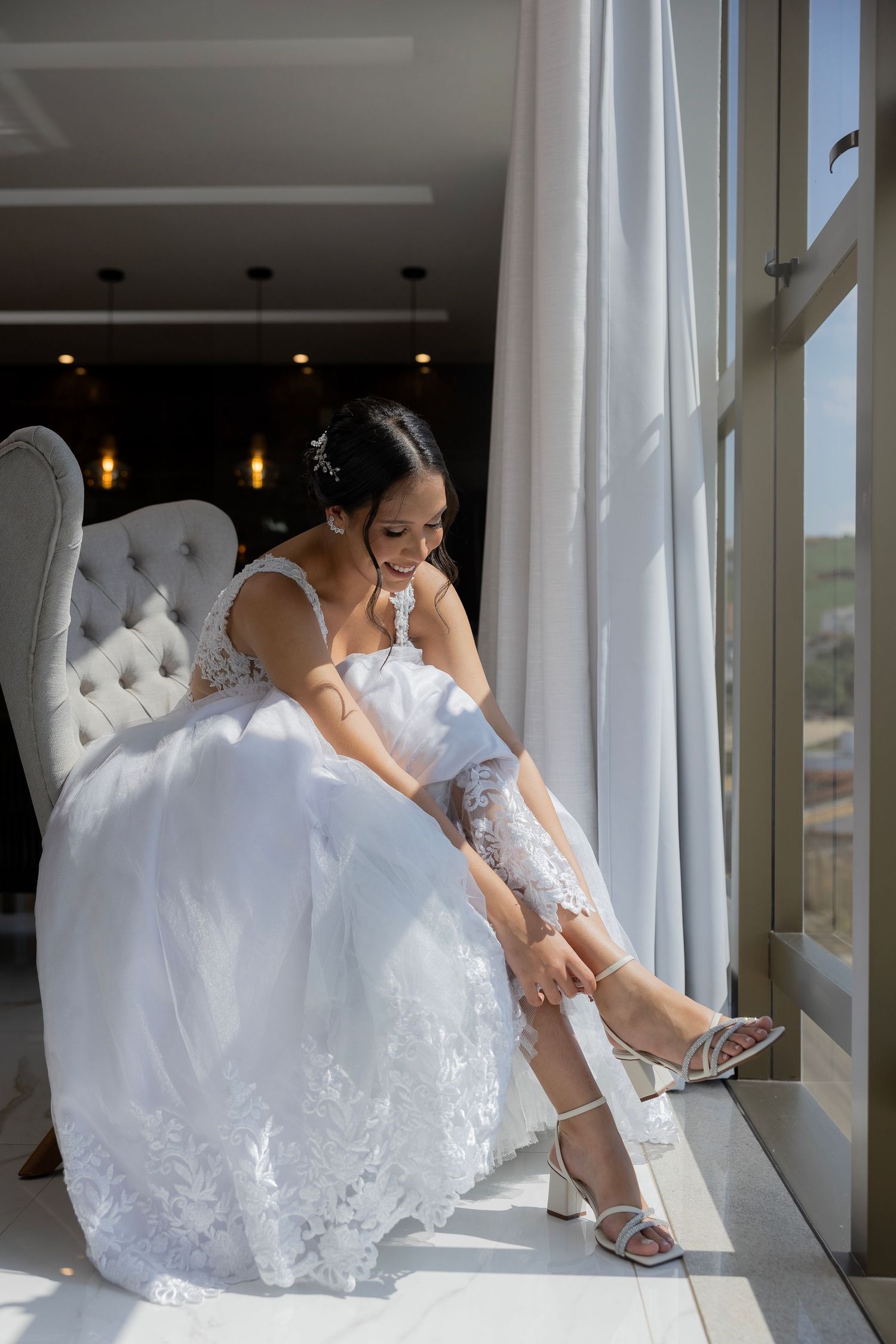 Bride putting on white heels by a sunlit window while getting ready for her wedding in Florida