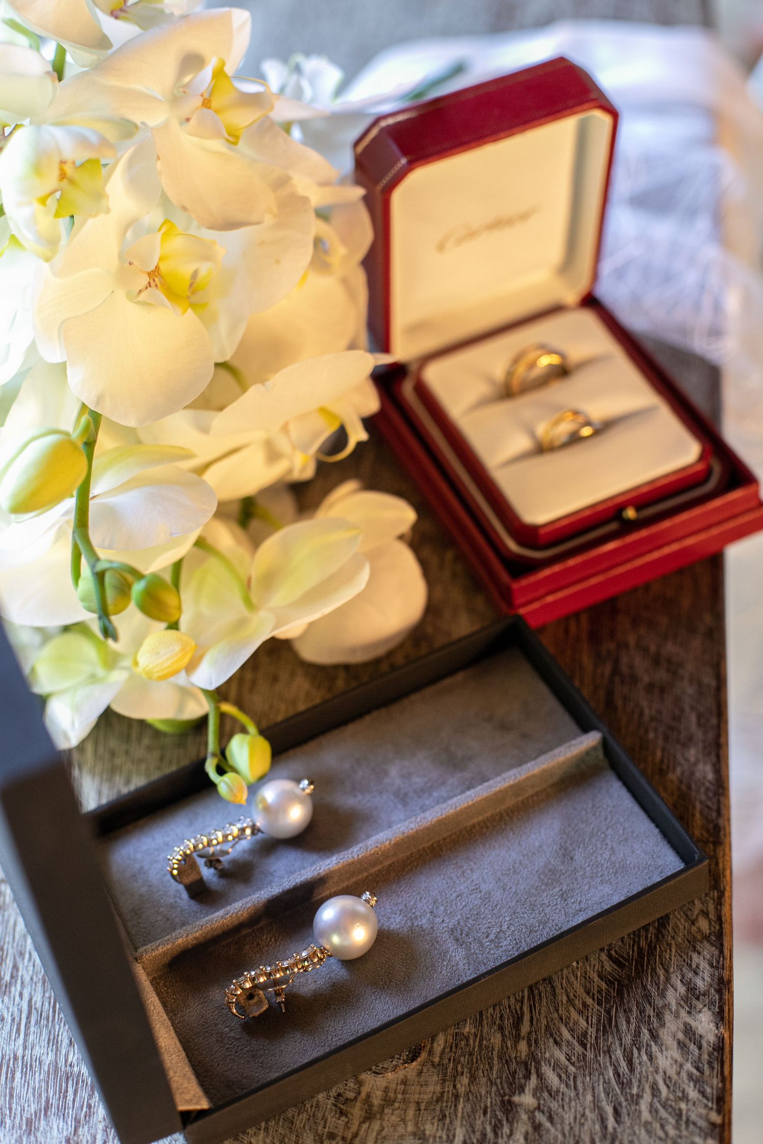 Wedding rings and white flowers displayed in red jewelry boxes on a wooden surface.