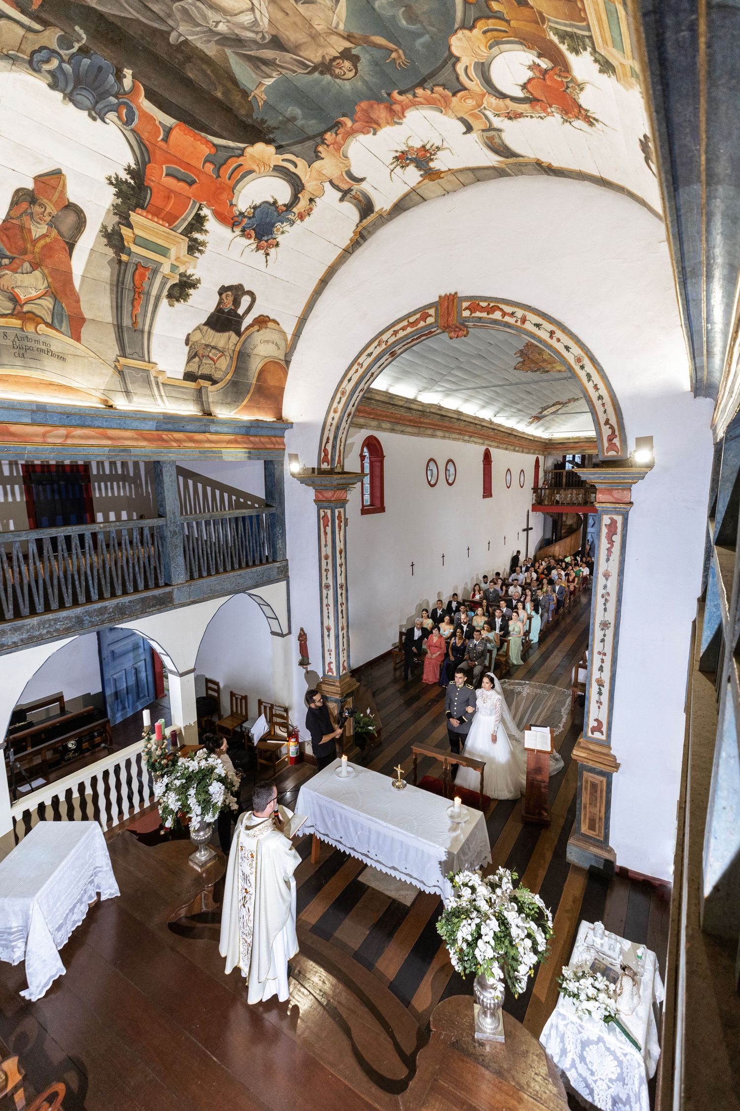 Historic church interior with ornate ceiling frescoes and wooden railings during a wedding ceremony.