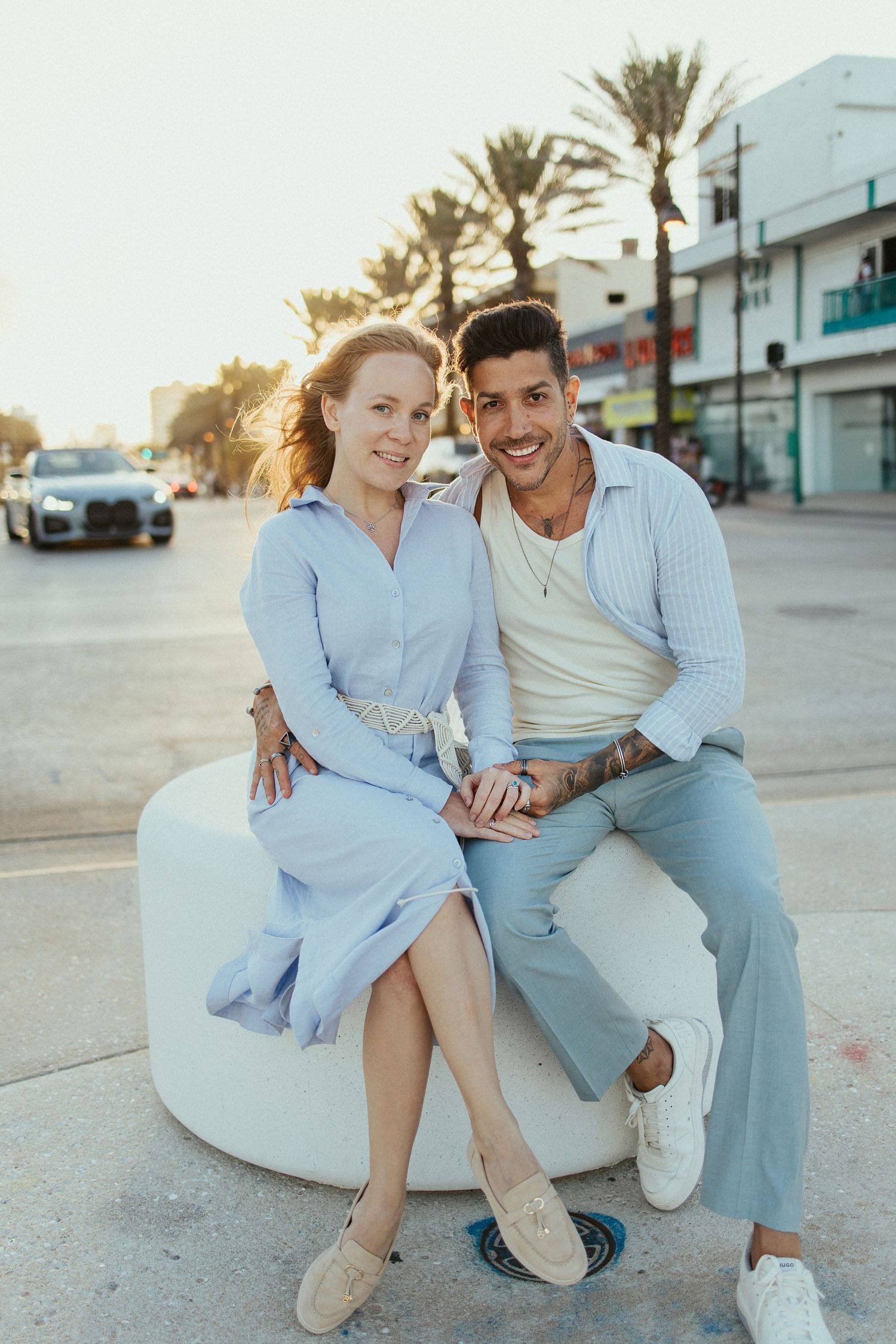 Casual couple photoshoot in light blue outfits on urban street at sunset.