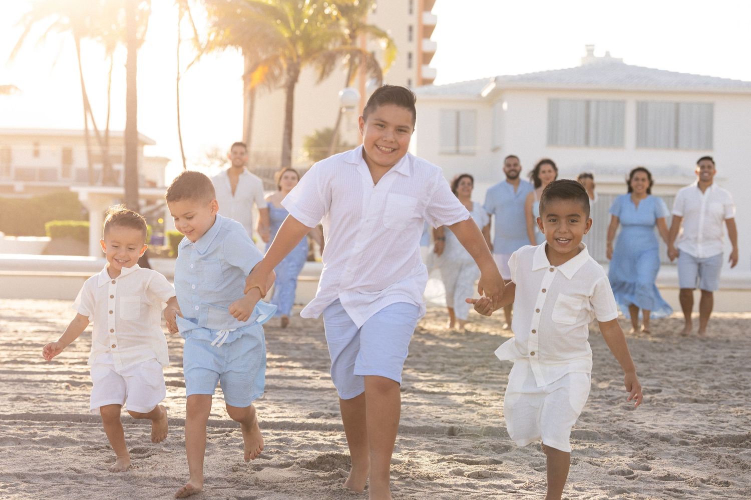 Family enjoying a playful moment together on a sunny beach at sunset with palm trees in the background.