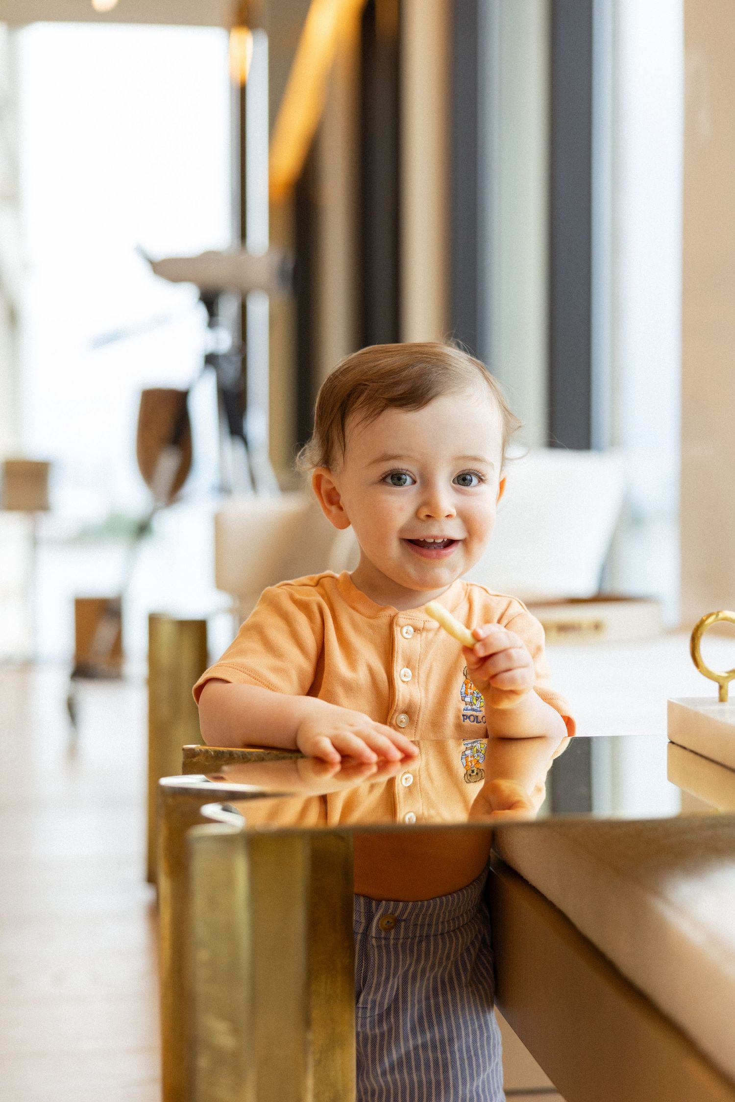 A small child in a peach-colored shirt leans against a counter in a bright, modern space.