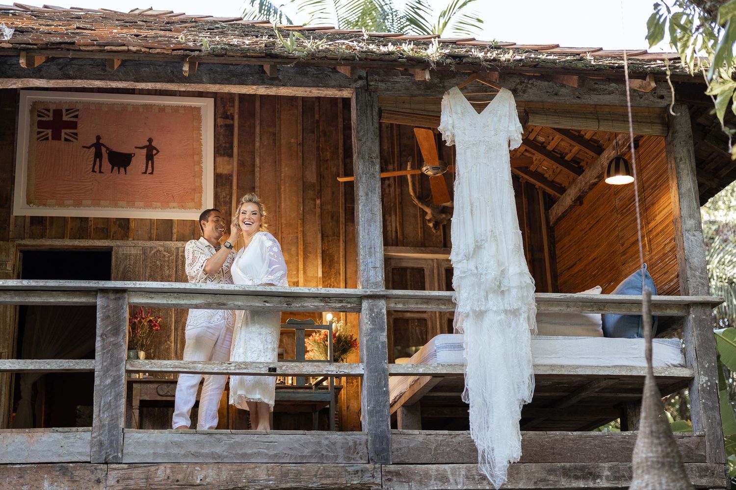A wedding dress hangs on display at a rustic wooden venue with tropical surroundings.