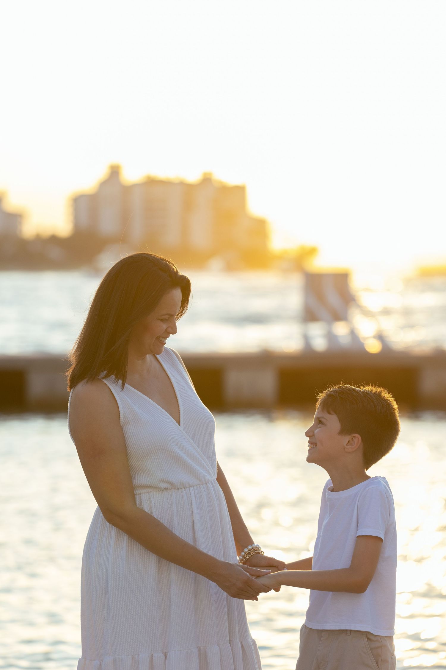 Mother and child silhouettes against sunset by the water sharing a tender moment.