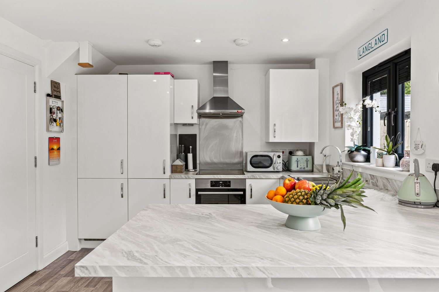 White modern kitchen featuring marble countertops, stainless steel appliances and fruit bowl centerpiece.