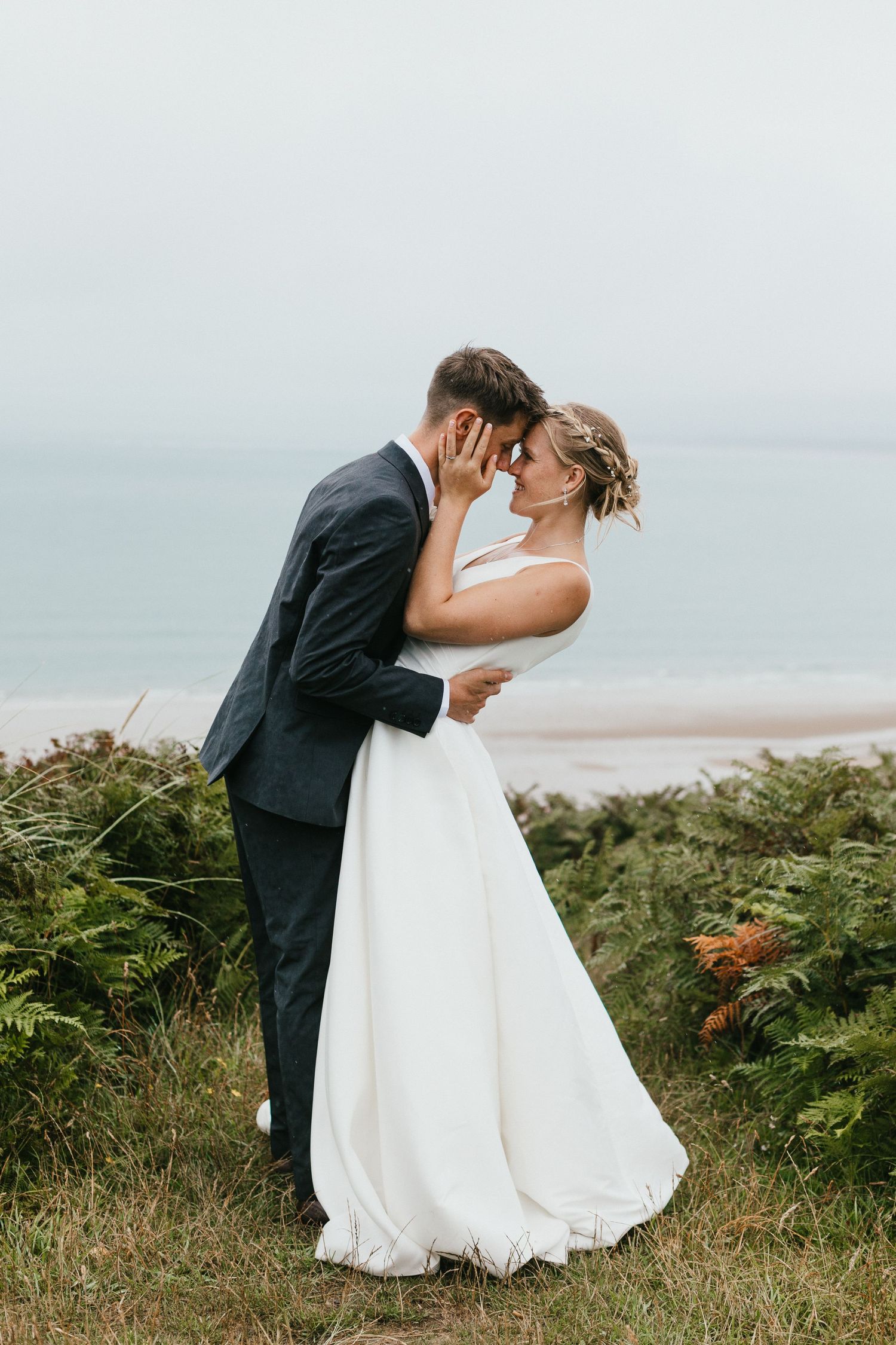 Intimate wedding photo on a coastal cliff with couple embracing in formal attire.
