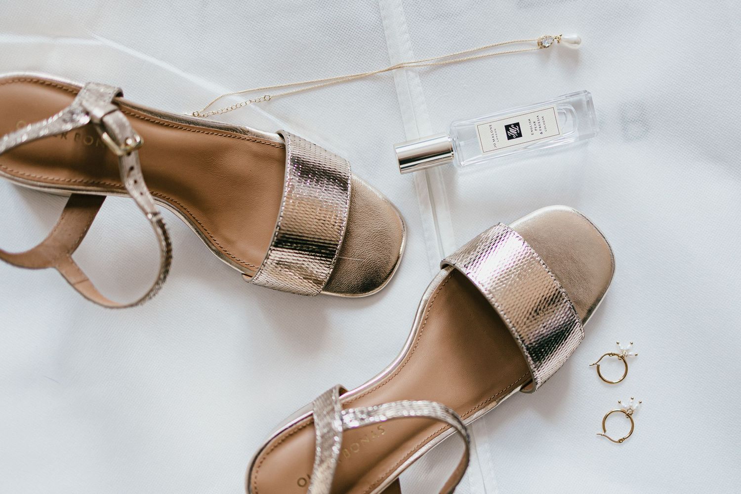 Metallic wedding sandals with rings displayed on white fabric.