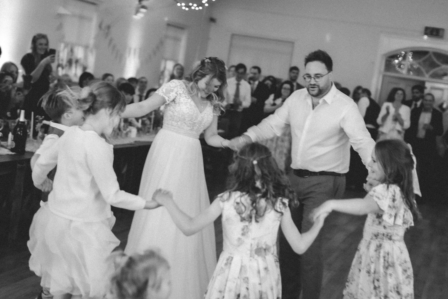 Wedding guests dance together in a joyful circle during a black and white reception celebration.