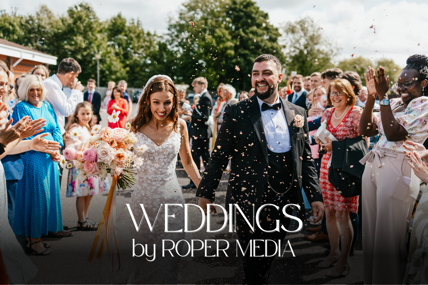 Joyful wedding celebration outdoors with confetti and guests in sunny garden setting.