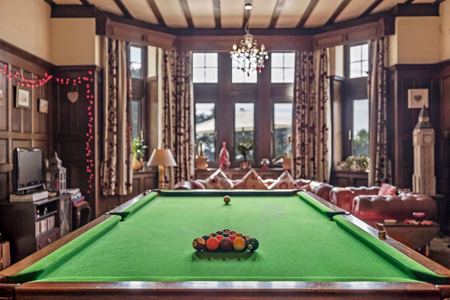 Elegant game room featuring a large green pool table with wooden beam ceiling and decorative windows.