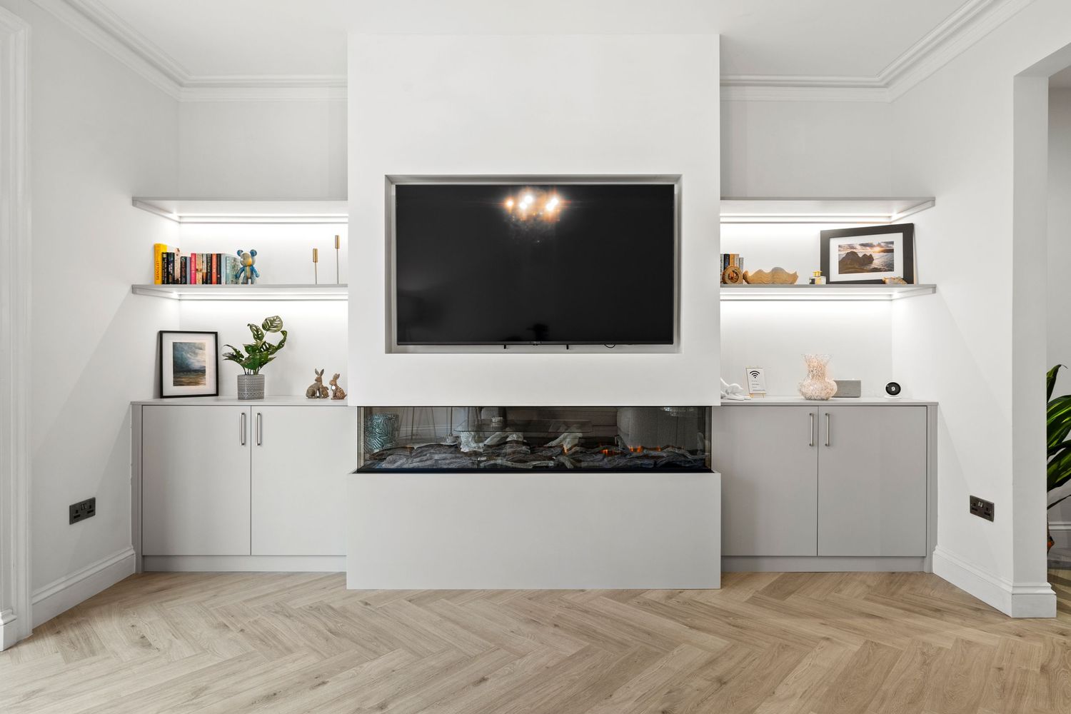 Modern living room with wall-mounted TV, built-in shelving, and herringbone wood flooring.