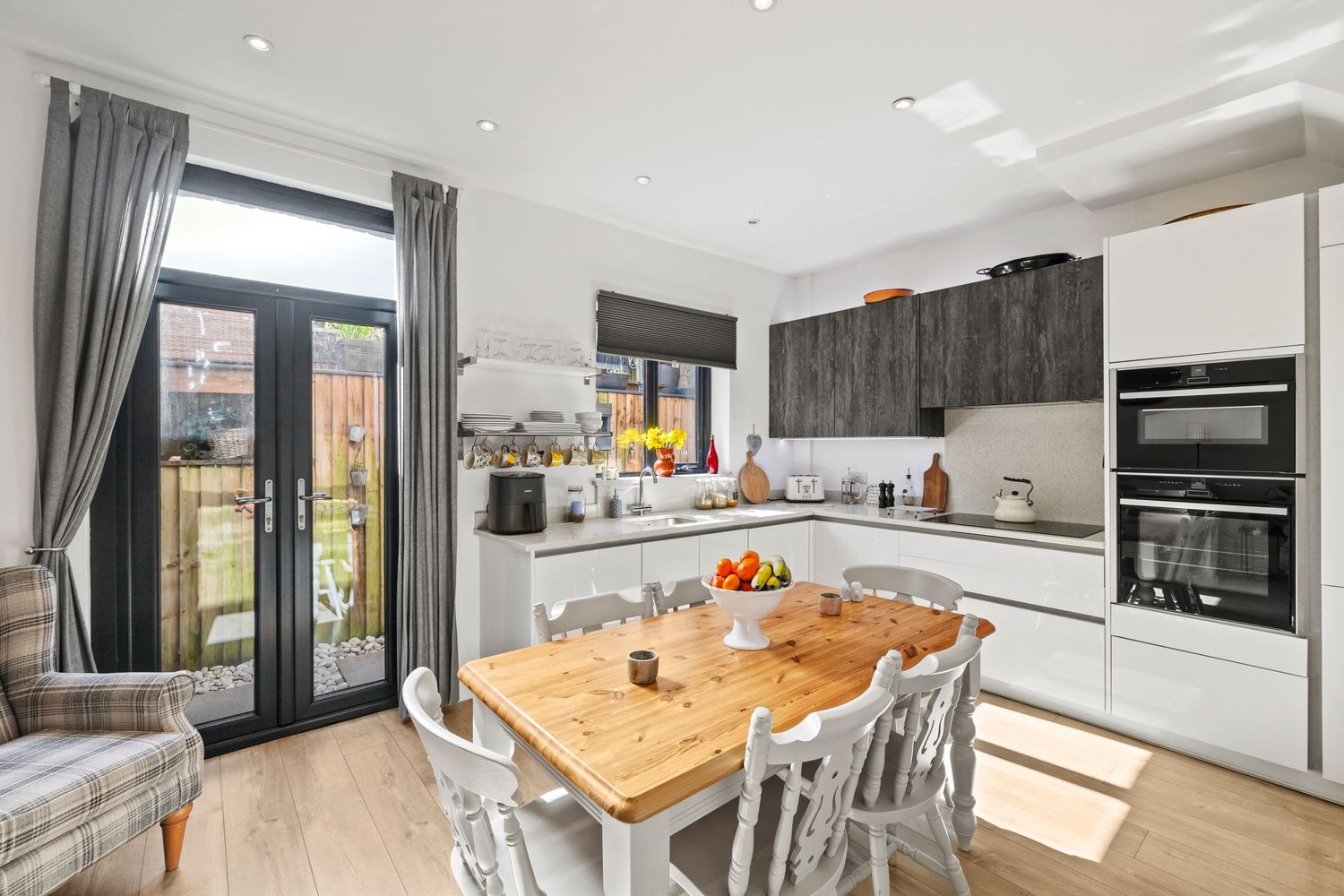 Modern open plan kitchen with white cabinets, wooden dining table and sliding glass doors to garden.