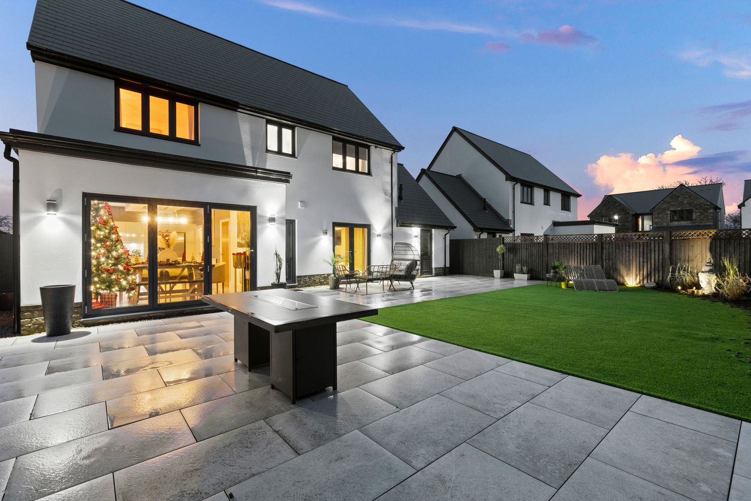 Contemporary house exterior featuring sleek patio furniture and modern landscaping with evening lighting.